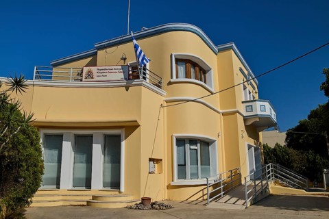A modern yellow building with balconies and Greek flag, artistically designed, Armando Bernabiti,