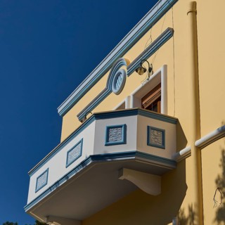Yellow building with decorative balcony in front of a clear blue sky, Armando Bernabiti,