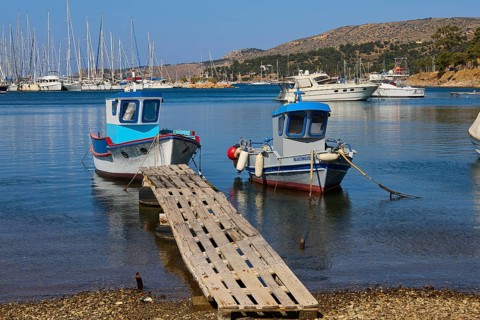 Two colourful boats on a wooden jetty with blue water and yachts in the background, Lakki, Leros,
