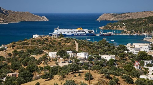 Large ferry in front of a coastal settlement on a hill with blue sea in the background, Lakki,