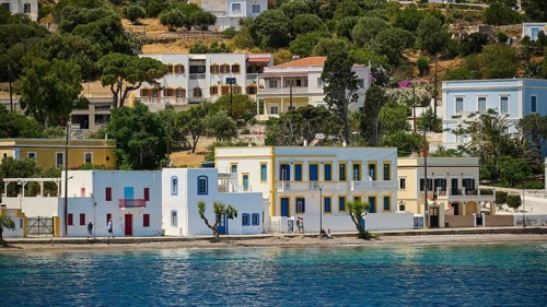 Colourful coastal houses with palm trees along a blue stretch of sea, Lakki, Leros, Dodecanese,