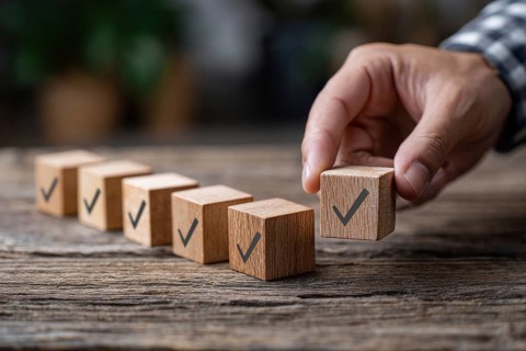 Checklist and task progress tracking concept. A hand placing the final checkmark on wooden blocks