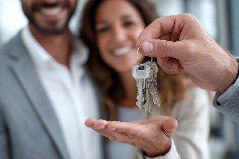 Close up of real estate agent giving house keys to happy couple. New property owners, american