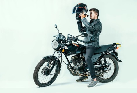 Man on motorcycle putting on helmet, isolated background. Young motorcyclist wearing safety helmet.