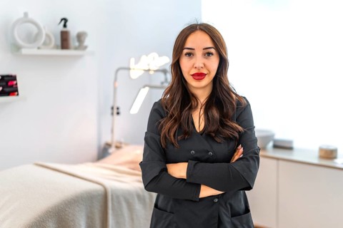 Confident female beautician standing with crossed arms in her modern beauty salon, representing