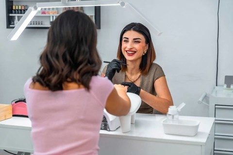 Smiling manicurist applying nail polish to her customer in a beauty salon, performing a