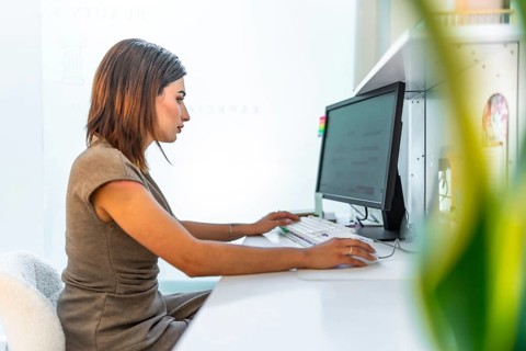 Beautician using a desktop computer, managing appointments and customer data in a bright and modern