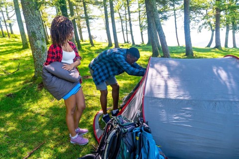 Couple setting up a tent in a lush forest, preparing their campsite for a summer adventure filled