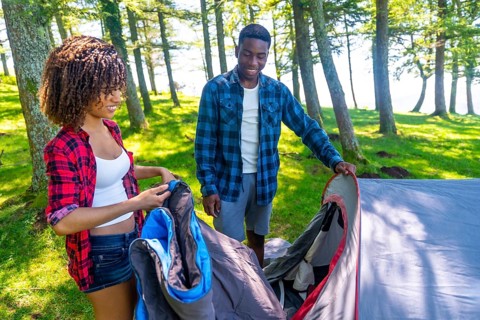 Young black couple setting up their tent in a forest campground near a lake, enjoying a summer