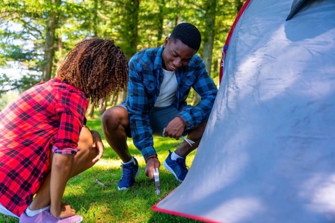 Young black couple setting up their tent in a serene forest, embracing the joy of camping and