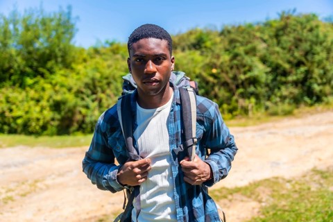 Confident young hiker wearing a backpack, enjoying a sunny day while discovering a beautiful nature