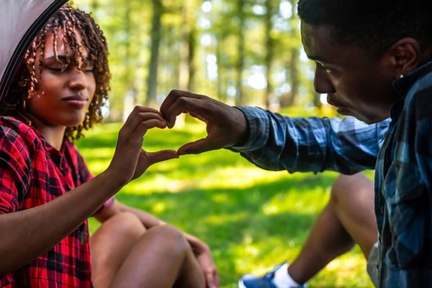 Happy couple making heart shape with hands while camping in nature, enjoying a romantic moment