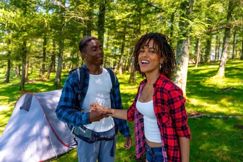 Happy smiling backpackers holding hands near tent in the woods, enjoying summer vacation camping