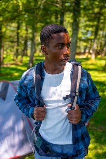 Young hiker wearing backpack exploring forest near campsite, enjoying outdoor adventure and