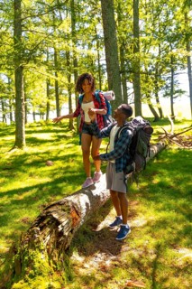 Young backpacking couple holding hands and balancing on a fallen tree trunk while hiking through a