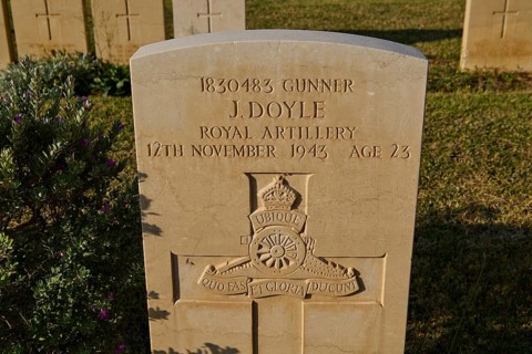 A single gravestone with inscription near grass and shade in a cemetery, J. Doyle, Royal Artillery,