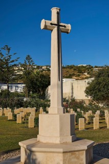 A high stone cross in a well-kept peaceful military cemetery under a clear blue sky, Military