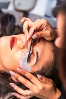 Beautician combing eyelashes with micro brush and applying individual lashes on client's upper