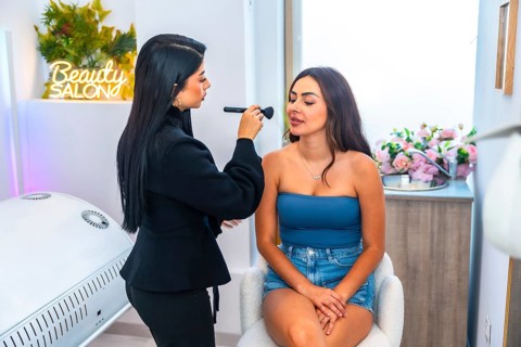 Beautician applying makeup with a brush on a young woman's face in a vibrant beauty salon,