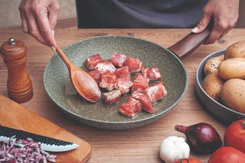 Diced pork meat, with vegetables, on a wooden kitchen table, in a cozy home environment