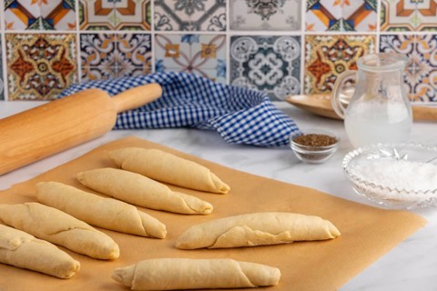 Rolled, raw pretzel sticks on baking paper with rolling pin and spices