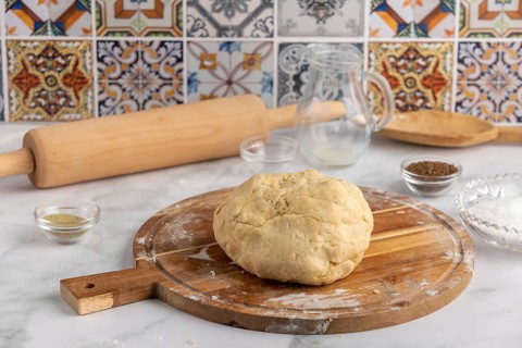 Dough on a wooden board with rolling pin and bowls in front of colourful tiles