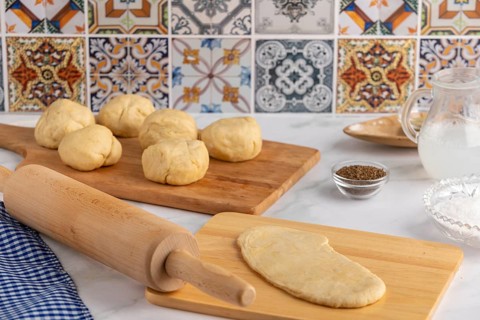 Dough balls on a wooden board with a rolled out dough, rolling pin next to it