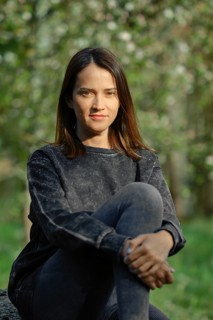 A young woman with long dark hair sits comfortably on a rock, wearing a casual sweater and leggings