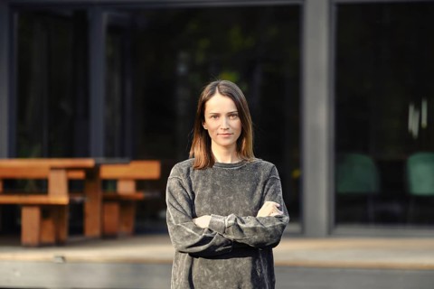 A young woman with shoulder-length hair stands confidently with her arms crossed outside a sleek,
