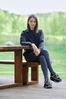 A young woman sits on a wooden bench beside a table, wearing casual attire. She enjoys the peaceful