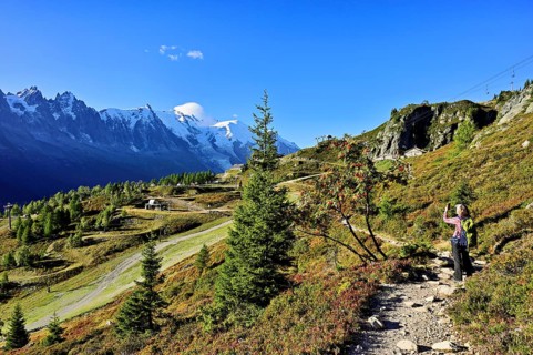 Female hiker on a hiking trail with the La Flégère cable car mountain station and the snow-covered