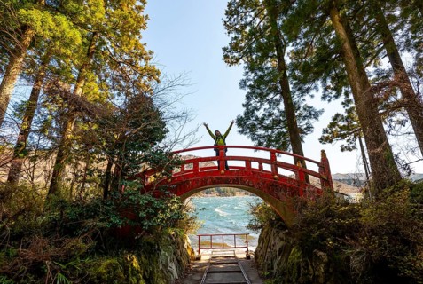 Young man walking on red bridge, path along Lake Ashi to Hakone shrine, Hakone, Japan