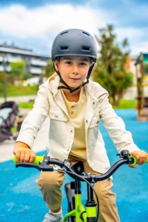 Young boy wearing a helmet rides a bicycle in a park, enjoying a sunny day outdoors while promoting