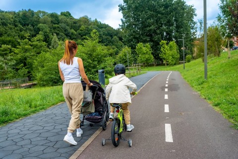 Mother pushing stroller and child riding bicycle on a paved path in a park, enjoying quality family