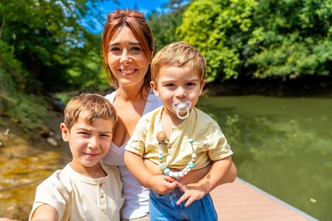 Mother and her two sons enjoying a sunny day by the river, capturing a joyful selfie while smiling