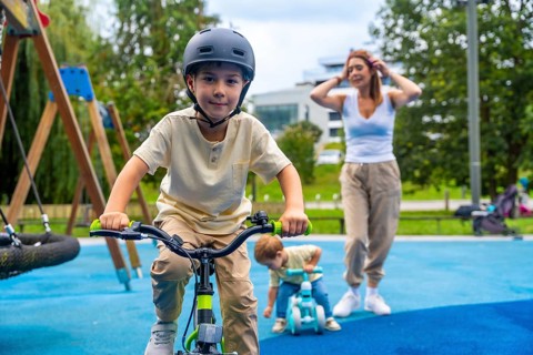 Happy children enjoying riding bicycles in a modern playground while their mother watches over