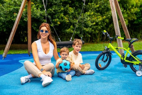 Happy mother sitting with her two sons on a playground's blue rubberized surface near a bicycle and