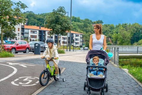 Mother pushing a baby stroller while her son rides a bicycle on a bike path in a modern urban