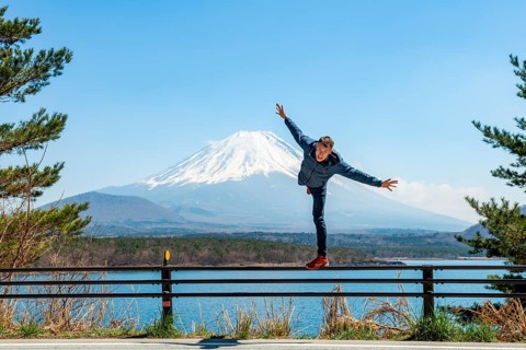 Young man balancing on railings next to a road, view across the lake to Mt Fuji volcano, Motosu