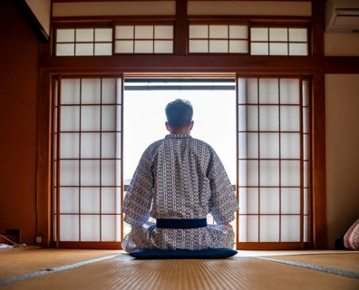Young man wearing kimono sitting in traditional Japanese living room with tatami mats and shoji