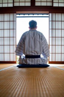 Young man wearing kimono sitting in traditional Japanese living room with tatami mats and shoji