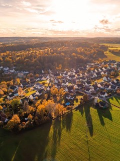 Idyllic village in autumn light with many houses and surrounding fields, surrounded by forests,