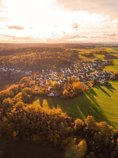 Autumn landscape with a village flooded with warm light, surrounded by fields and forests,