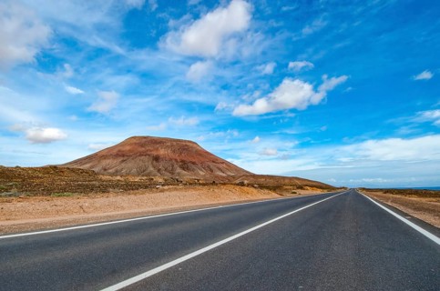 View of long straight paved road to the left partly eroded volcano volcanic cone in volcanic