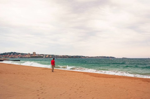 Man wearing a red shirt looking at the moving sea, Fréjus in the background, Provence-Alpes-Côte