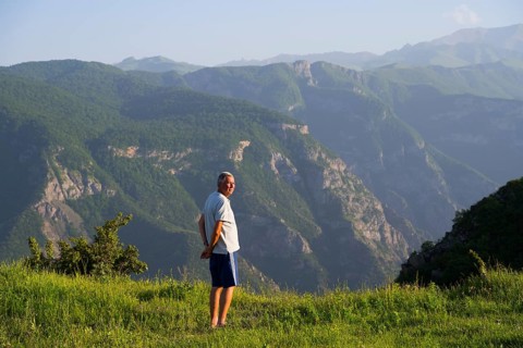 Man standing in a green field with a view of majestic mountain landscape and valley of the Vorotan