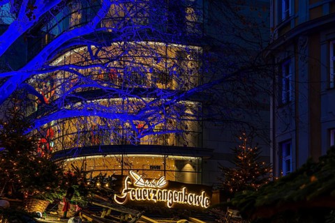 Sales stand for Feuerzangenbowle, above a deciduous tree illuminated with blue light,