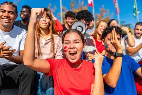 Diverse young people cheering excitedly at a stadium, wearing team colors and face paint while