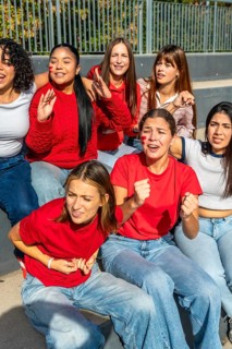 Group of diverse young women friends wearing red shirts and face paint, sitting together and