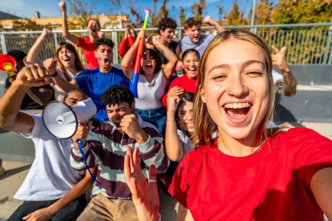 Young diverse fans cheering and taking a selfie in sunny stadium stands, celebrating their team